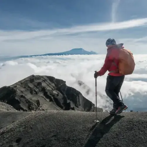 A male hiker is descending after sunrise at the edge of the crater from the summit of Mount Meru (4.562 mt,, 14.967 ft.) in Tanzania. The area is famous for hiking and to get accl…